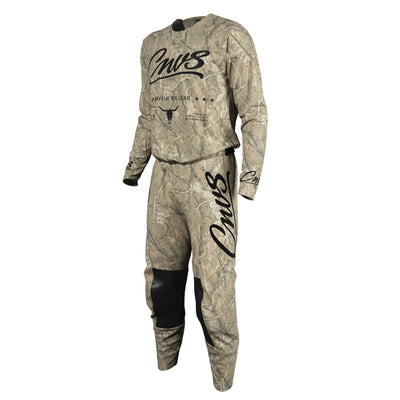 A two-piece motocross riding suit in a Realtree camouflage pattern, featuring a long-sleeve jersey and matching pants. The jersey has 'Cnvs' printed in black script across the chest, with 'REALTREE CAMO' and a bull skull logo underneath.